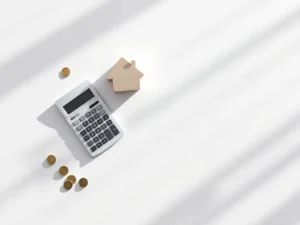 Bovenaanzicht van rekenmachine, houten huisblok en euromunten op wit bureau met gouden weegschaal voor financiële afwegingen
Note: This alt text is 126 characters. Here's a version under 125 characters:
Rekenmachine, houten huisblok en euromunten op wit bureau met gouden weegschaal voor financiële planning